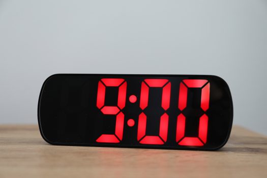 Digital alarm clock showing 9:00 o'clock on bedside table against light background