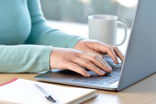 Cropped shot of a student hands writing in a gray laptop at home